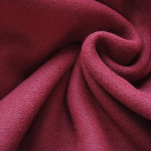 May include: Close-up of a deep burgundy fabric with a soft, textured surface. The material is draped in gentle folds, creating shadows and highlights that emphasise its plush appearance. The fabric's colour is consistent throughout, suggesting a high-quality textile.
