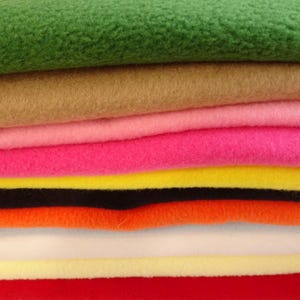 May include: A selection of colourful fleece fabric in shades of green, brown, pink, yellow, orange, and red. The soft, textured material is arranged in horizontal layers, displaying the different colours and textures.
