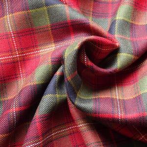 May include: A close-up shot of a folded fabric with a tartan pattern. The fabric is predominantly red, with intersecting lines in white, yellow, green, and navy. The texture of the material is visible. The overall aesthetic is traditional, suitable for clothing or home furnishings.