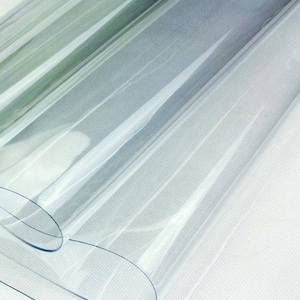 May include: A close-up of a clear, transparent plastic sheet with a slight blue tint. The sheet has a smooth surface and is slightly curved, with visible lines and folds. The background is a white, textured fabric.