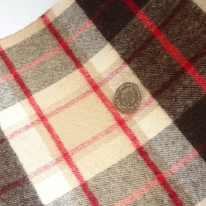 May include: A close-up of a brown, beige and red plaid fabric with a British one-pound coin on top. The coin features a profile of Queen Elizabeth II.