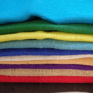 May include: A selection of coloured burlap fabric samples, including blue, green, yellow, and red. The rough texture of the fabric is evident, with each layer displaying a different shade. The arrangement offers a visual display of colour choices for craft projects.