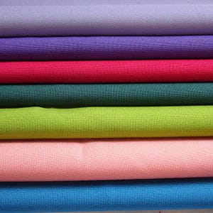 May include: A selection of fabric swatches in a range of colours, including lavender, purple, red, green, lime green, pink, and blue. The fabric has a tight weave, possibly cotton or a similar textile.