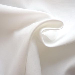 May include: Close-up of white fabric with gentle folds and a smooth texture. The fabric appears lightweight and flowing, with highlights and shadows creating depth. The overall impression is of a delicate, luxurious material.