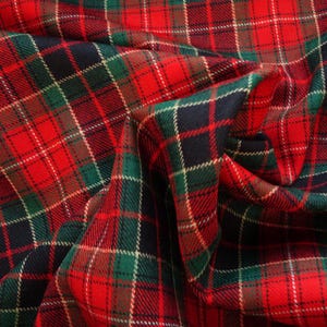 May include: A close-up shot of a folded fabric with a traditional tartan pattern. The fabric is predominantly red, with intersecting lines of green, navy, and white. The material has a textured finish, with visible woven threads.