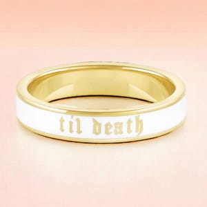 Puede incluir: Anillo dorado con una banda de esmalte blanco. El anillo presenta la frase "til death" en una fuente gótica. Esta joya es adecuada para el uso diario o como accesorio para ocasiones especiales.