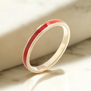 May include: A thin gold band ring with a single red enamel stripe around the center.