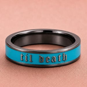 May include: A black ring with a turquoise band featuring the phrase "til death" in a gothic font. The ring has a sleek, modern design, suitable for everyday wear.