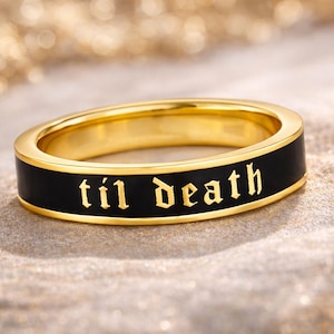 May include: A gold ring with a black band. The words "til death" are inscribed in gold lettering on the black band. The ring is set against a textured, golden background.