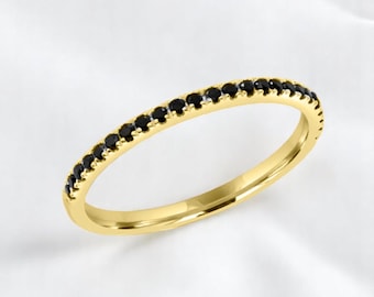 May include: A gold ring featuring a line of small, black gemstones. The ring's polished gold band contrasts with the dark stones, set against a white backdrop. The ring is a piece of jewellery.