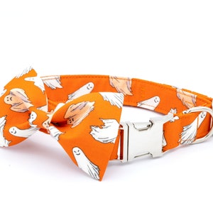 May include: Orange dog collar and bow tie set with a repeating pattern of white cartoon ghosts. The collar has a silver metal buckle and a D-ring. The bow tie is pre-tied and attached to the collar. Perfect for Halloween.