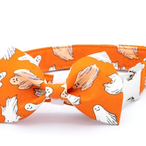 May include: Orange dog collar and bow tie set with a white ghost pattern. The collar has a silver-colored metal buckle and a matching bow tie. A festive accessory for Halloween or themed events.