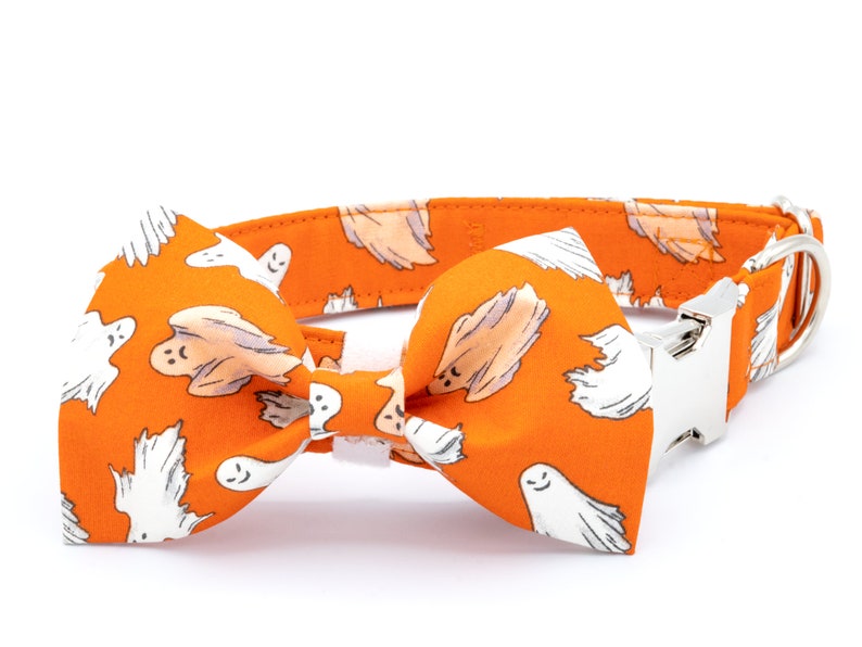 May include: Orange dog collar and bow tie set with a white ghost pattern. The collar has a silver-colored metal buckle and a matching bow tie. A festive accessory for Halloween or themed events.