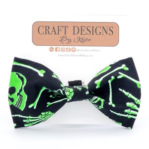May include: A black bow tie with a green skeleton pattern. The bow tie is made of fabric and has a black adjustable strap. The bow tie is a fun and festive accessory for Halloween.