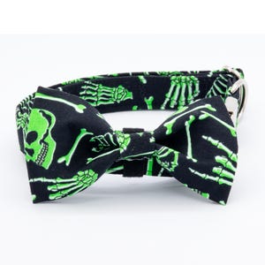 May include: A black dog collar with a green skeleton print and a matching bow tie. The bow tie has a skull design.