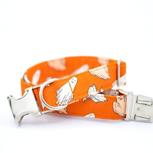 May include: An orange dog collar with a white ghost pattern. The collar has a silver metal buckle and D-ring. The fabric is a bright orange with white ghost illustrations. The collar is designed for pets.
