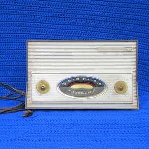 May include: A white vintage radio with a black dial and gold knobs. The radio has the text "MILTERAMIC" on the dial and "SUPER SELECTOR" on the top.