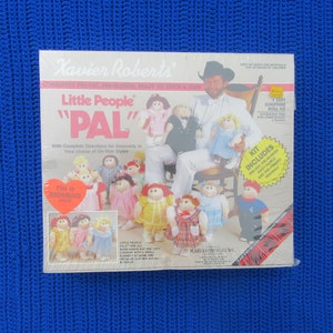 May include: A box for a Little People "PAL" doll kit. The box features a photo of a man holding a doll and a group of dolls. The box includes the text "Little People" and "PAL".