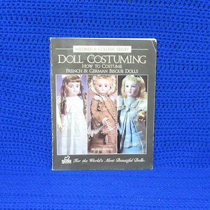 May include: A softcover book titled Doll Costuming: How to Costume French & German Bisque Dolls by Mildred & Colleen Seeley. The black cover features three photographs of dolls in historical attire and the text For the World's Most Beautiful Dolls.