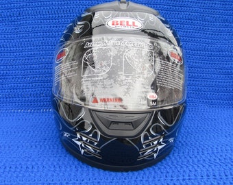 May include: Black motorcycle helmet with a white and gray design. The helmet has a clear visor with a warning label and the text "Arrow Helmet Faceshield". The helmet has a Bell logo and the text "Bell Helmets".