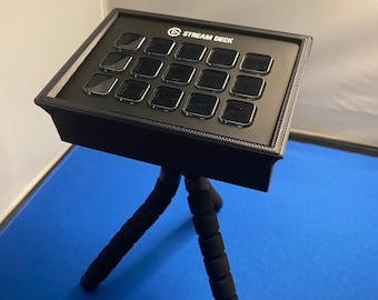 Puede incluir: Un Stream Deck negro con 15 botones está montado en un trípode negro. El trípode tiene tres patas con acolchado de espuma negra.