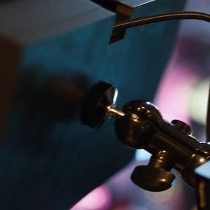 May include: A black metal camera mount with a ball head and a knob for adjusting the angle. The mount is attached to a blue surface.