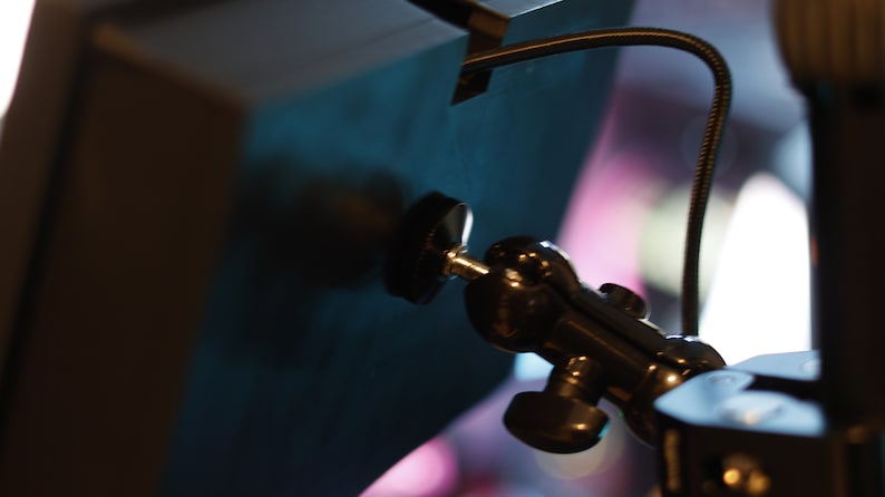 May include: A black metal camera mount with a ball head and a knob for adjusting the angle. The mount is attached to a blue surface.