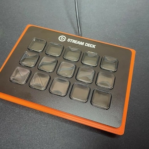 May include: A black Stream Deck with 15 customizable buttons, each with a clear plastic cover. The deck has an orange border and is connected to a computer via a USB cable.