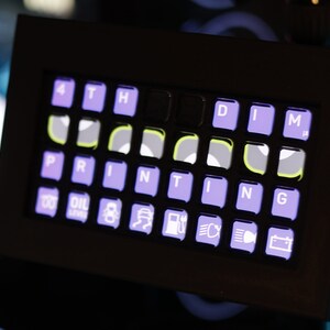 May include: A black control panel with a purple and white keyboard labeled "PRINTING" and a row of icons below the keyboard. The icons include a gas pump, a car battery, and a car with headlights.