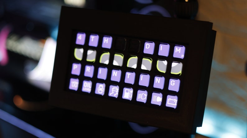 May include: A black control panel with a purple and white keyboard labeled "PRINTING" and a row of icons below the keyboard. The icons include a gas pump, a car battery, and a car with headlights.