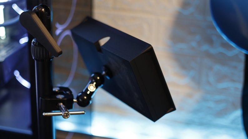 May include: A black tablet screen mounted on a black adjustable arm with a silver knob. The arm is attached to a black tripod stand with a silver knob.