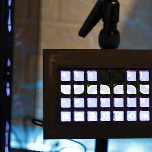 May include: A black framed keyboard with white keys and a light blue backlight. The keys are labeled with letters and symbols, including "PRINTING".