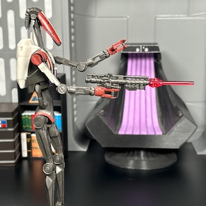May include: A red and gray action figure of a robot holding a blaster with a red beam. The robot has a white chest piece and is posed in a firing stance.