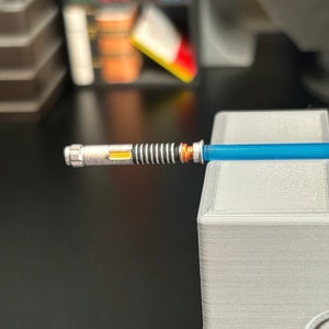 May include: A silver lightsaber with a blue blade and a yellow light inside the hilt.