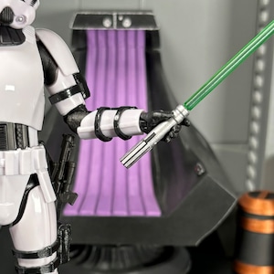 May include: A white and black action figure of a Star Wars Stormtrooper holding a green lightsaber. The figure is posed with its right arm extended, holding the lightsaber in a fighting stance.