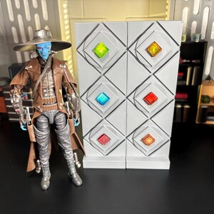 Op de afbeelding: Een blauwe en bruine action figure van een personage met een hoed en een lange jas staat voor een witte muur met zes kleurrijke vierkante panelen.