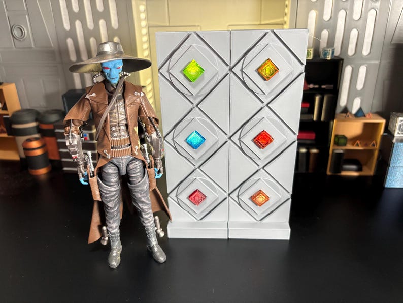 Op de afbeelding: Een blauwe en bruine action figure van een personage met een hoed en een lange jas staat voor een witte muur met zes kleurrijke vierkante panelen.