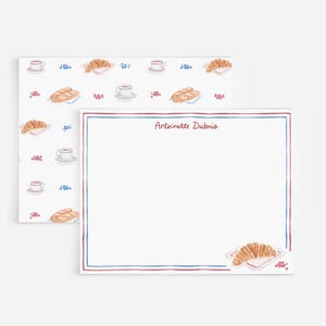 May include: A rectangular stationery sheet with a red and blue border, featuring the name Antoinette Dubois in red script at the top and a croissant illustration in the corner, paired with a matching patterned envelope with coffee and pastry icons.