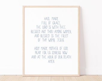 May include: A printable wall art print with the text "Hail Mary, full of grace, the Lord is with thee Blessed art thou among women, and blessed is the fruit of thy womb, Jesus Holy Mary, Mother of God, pray for us sinners now and at the hour of our death Amen" in a light blue font on a white background.