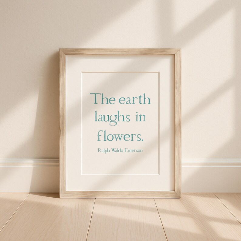 May include: A framed print featuring the quote "The earth laughs in flowers" in teal lettering, attributed to Ralph Waldo Emerson. The frame is light wood, and the print has a white mount.