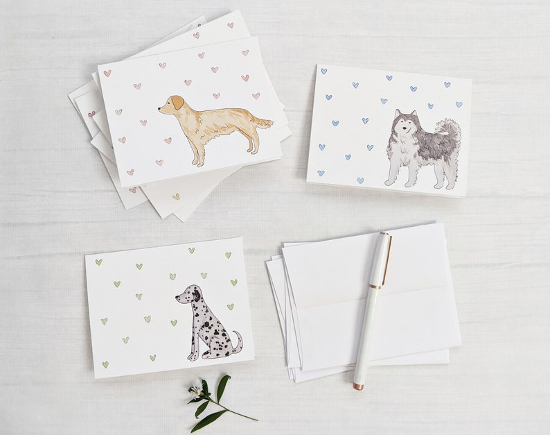 Peut inclure: Quatre cartes de v&oelig;ux vierges illustrant diff&eacute;rentes races de chiens. Les cartes ont un fond de petits c&oelig;urs roses, bleus ou verts. Les chiens sont un golden retriever, un husky, un dalmatien et un terrier.