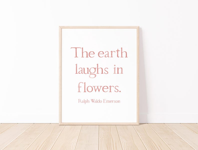 May include: A framed print featuring the quote "The earth laughs in flowers" in a soft pink font. The quote is attributed to Ralph Waldo Emerson. The frame is light wood, and the background is white.