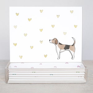 Peut inclure: Un ensemble de 8 cartes de v&oelig;ux vierges illustrant un beagle en aquarelle sur fond de c&oelig;urs jaunes. Les cartes sont emball&eacute;es dans une bo&icirc;te en plastique transparente avec un motif de c&oelig;urs roses et verts.
