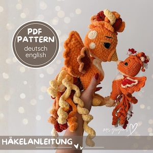 Könnte beinhalten: Gehäkelter Phönix und Küken in Orange-, Gelb- und Cremetönen. Der erwachsene Phönix hat große Flügel und einen langen, lockigen Schwanz. Das Küken ist kleiner und küsst den Erwachsenen. Der Text "PDF PATTERN deutsch english" und "HÄKELANLEITUNG" ist enthalten.