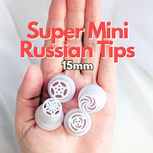 Puede incluir: Se muestran cuatro puntas rusas Super Mini blancas, cada una con un diseño decorativo único. Las puntas miden 15 mm. El texto "Super Mini Russian Tips" es rojo y el tamaño es verde.