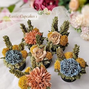 May include: Six cupcakes with buttercream floral decorations. The cupcakes feature various flower designs in shades of peach, yellow, and blue, with green foliage. The cupcakes are arranged on a white surface. The text "Rustic Cupcakes 1" is visible.