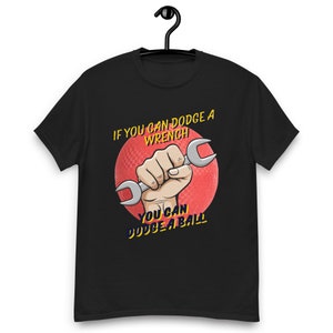 May include: Black t-shirt featuring a red and white graphic of a hand holding a wrench. The text on the shirt reads "If you can dodge a wrench you can dodge a ball."