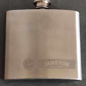 Può includere: Una fiaschetta in metallo argentato con tappo a vite. La fiaschetta ha il logo Jameson Irish Whiskey inciso sul davanti.