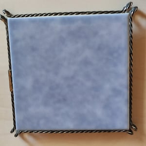 Könnte beinhalten: Eine kleine, rechteckige, blaue Keramikfliese mit Marmormuster ist in einem schwarzen Metallrahmen mit einem seilartigen Design gerahmt. Der Rahmen hat eine goldene Oberfläche.