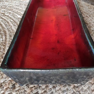 Peut inclure: Un pot rectangulaire en céramique avec un extérieur gris foncé et un intérieur rouge. Le pot a une surface texturée et un bord légèrement surélevé.